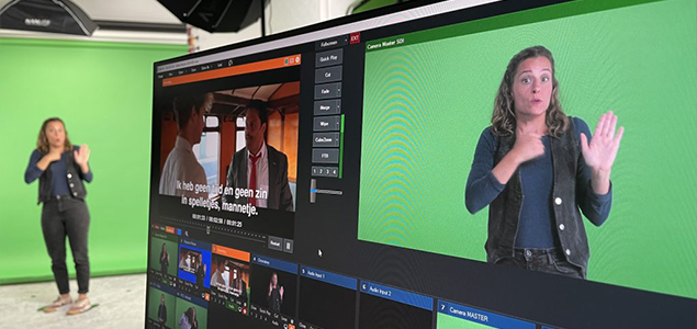 Monitor met videoproductiesoftware en een gebarentolk voor een groen scherm in een studio.